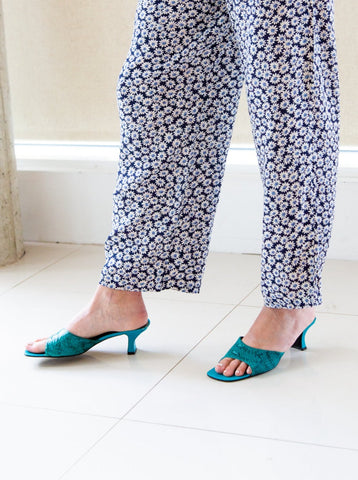 Woman wearing teal snakeskin mules and daisy-print trousers