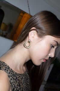 Model wears oversized gold door knocker earrings