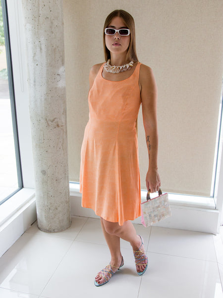 Woman wearing a vintage 1990s pastel orange sleeveless skater dress with strappy back.